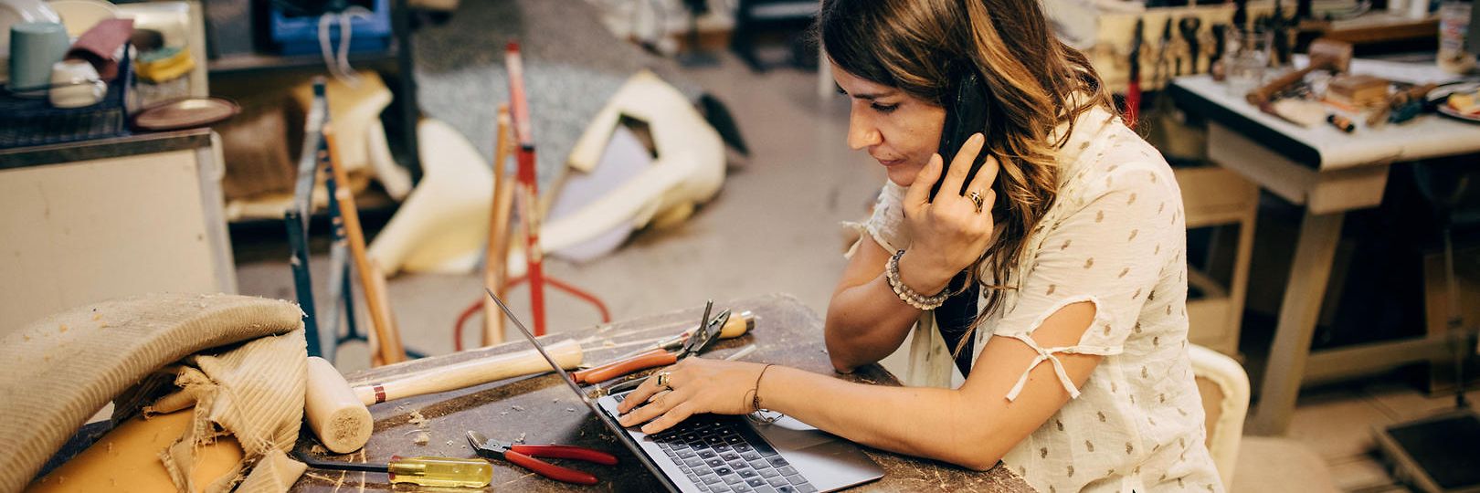 Frau in Werkstatt arbeitet mit Laptop und Telefon